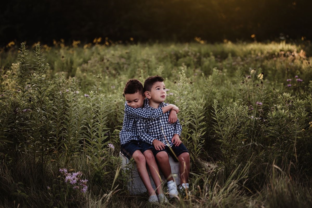 Two children in matching shirts sitting together in a wild meadow at golden hour.