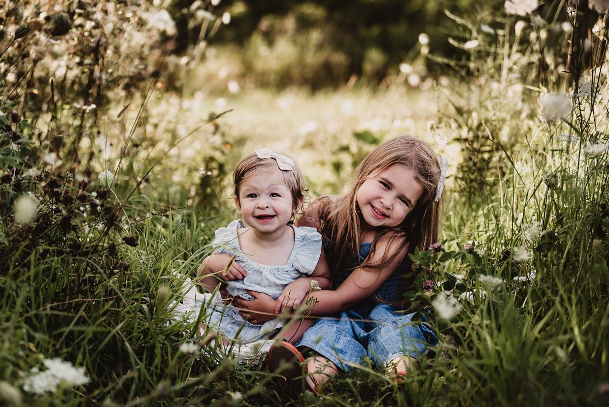 Two children sitting together in a sunlit meadow filled with wildflowers.