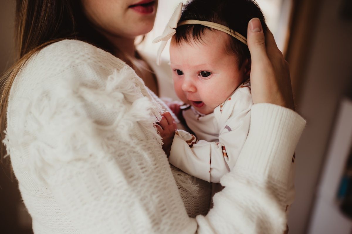 Parent in white sweater cradling infant in intimate indoor portrait.