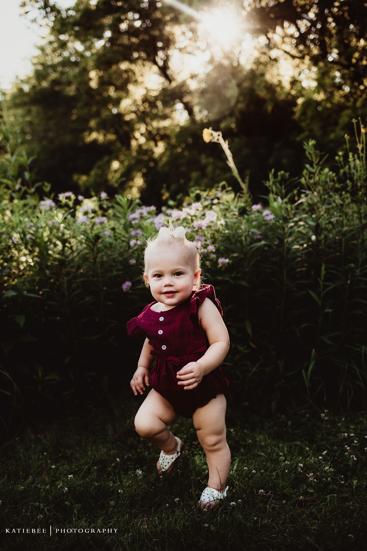 Toddler in burgundy romper running through garden at golden hour.
