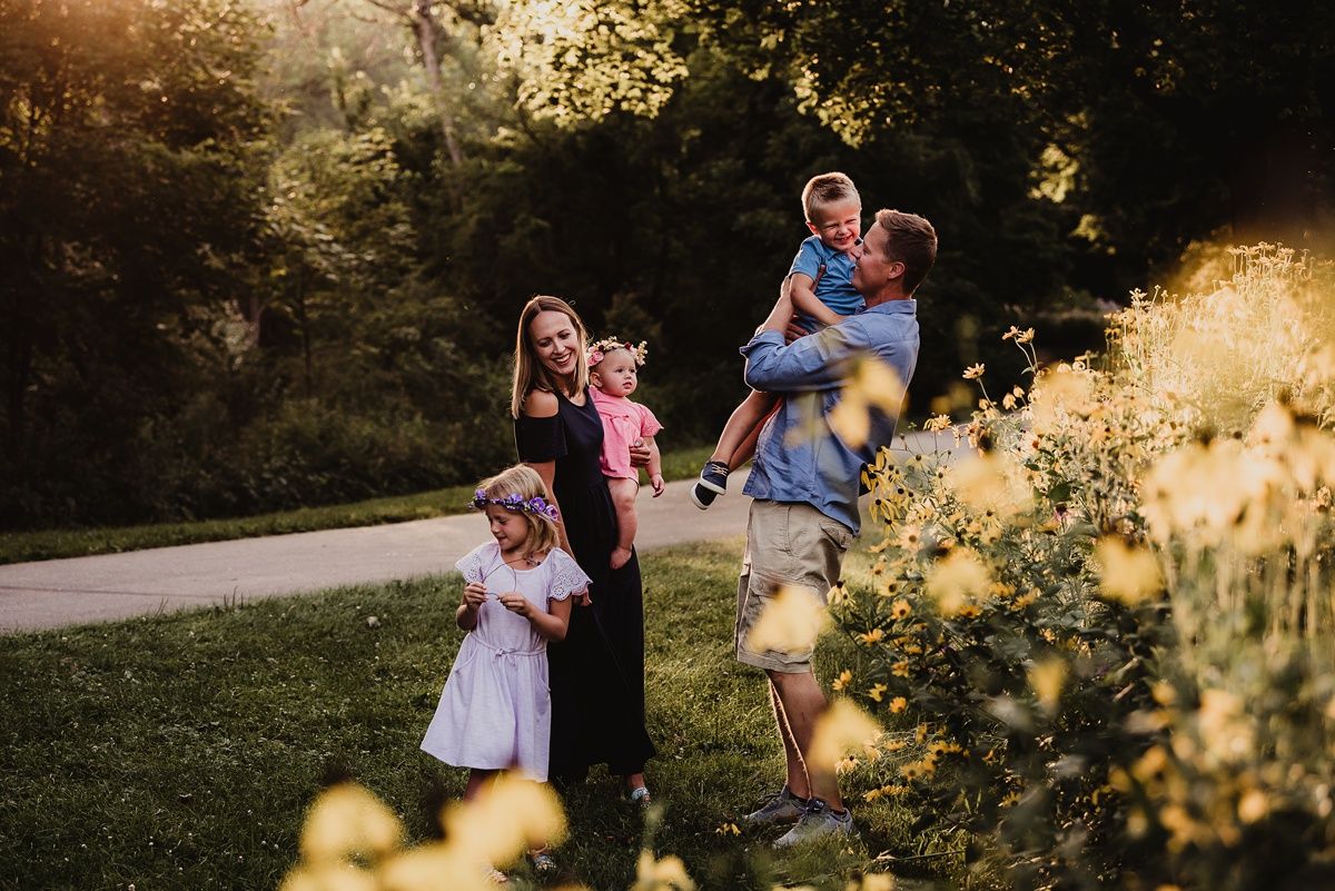 Family portrait session in a park during golden hour with blooming yellow flowers in foreground.