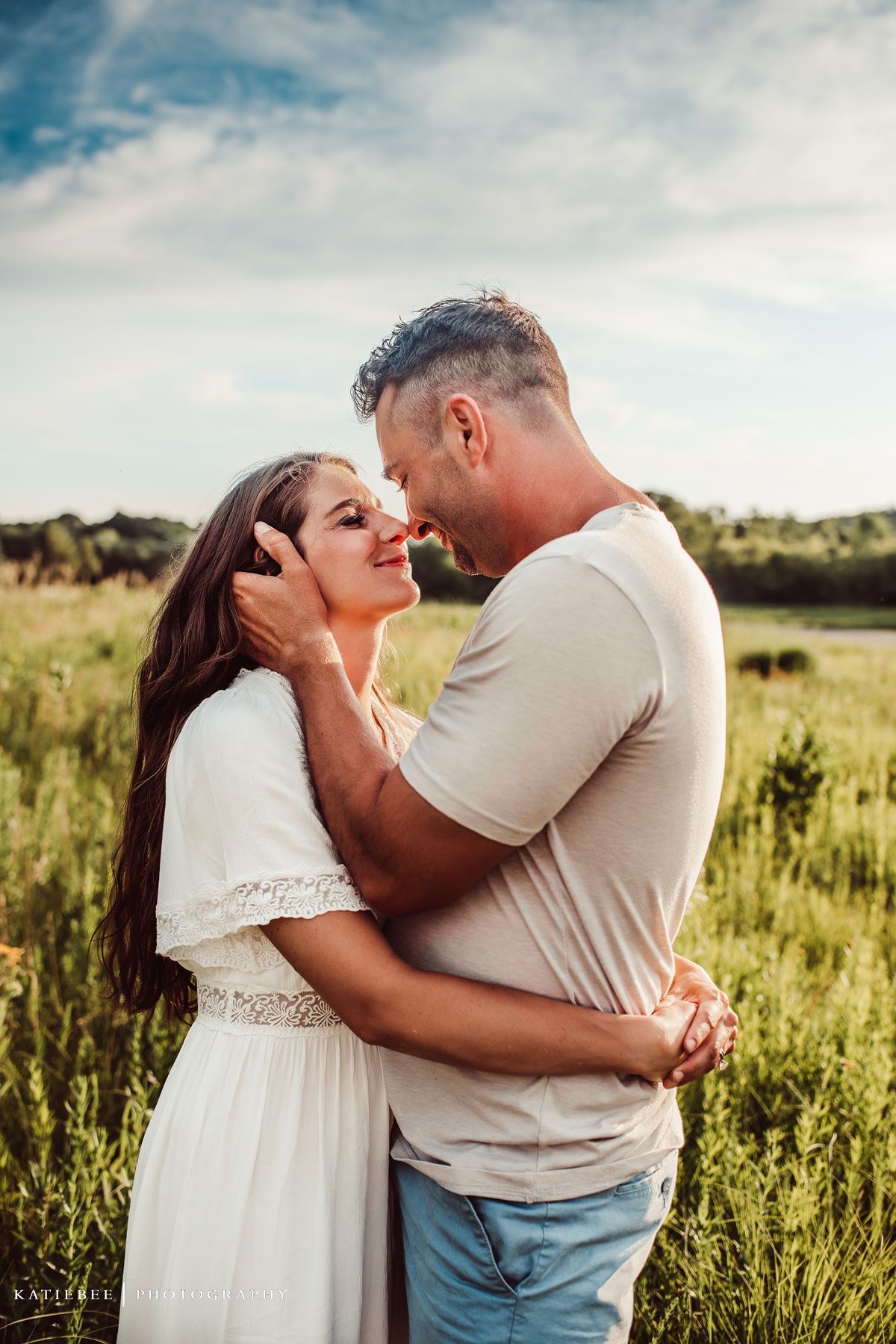 Intimate moment between couple in white dress and casual wear in sunny field.