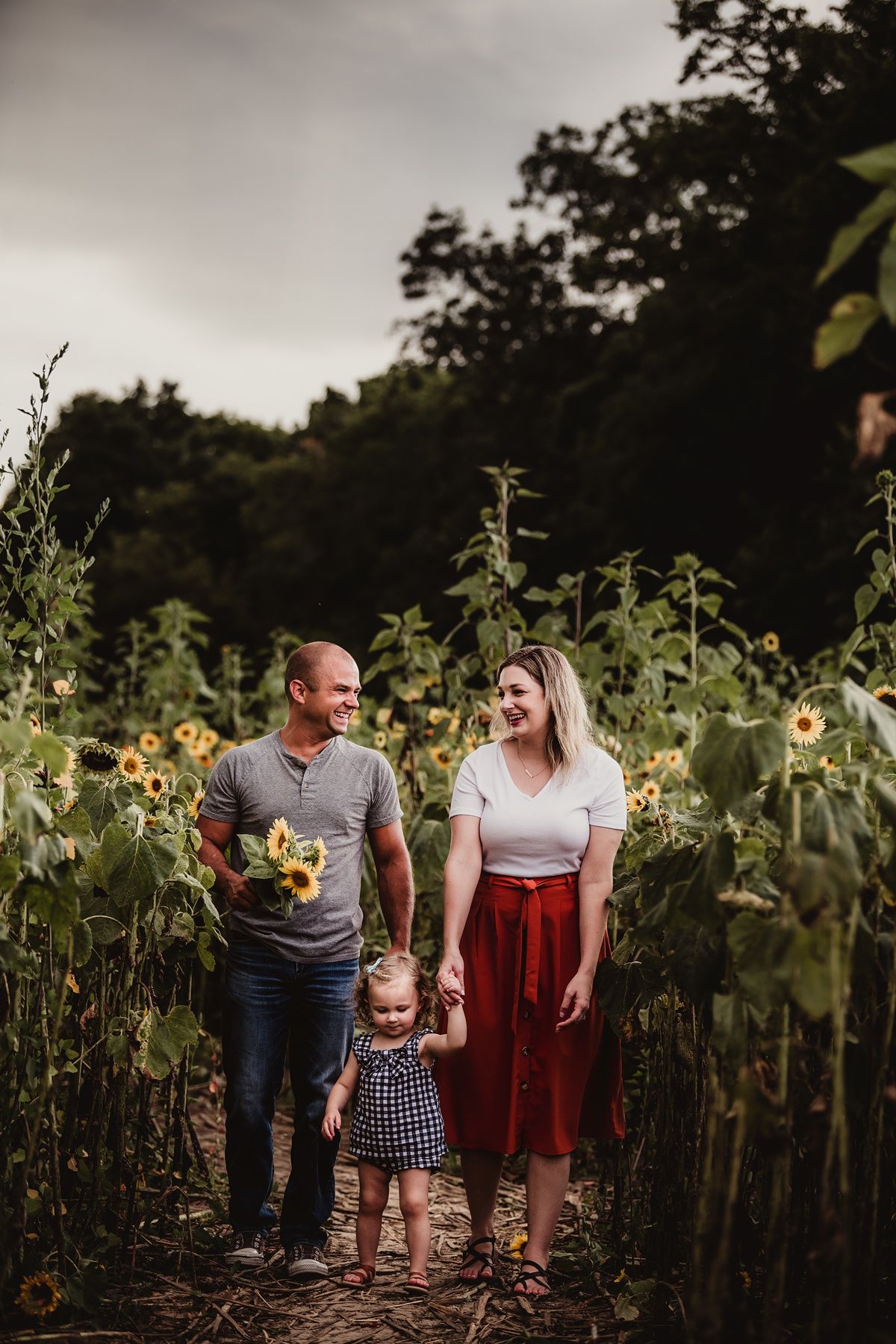Family walking together through towering sunflower field at dusk.
