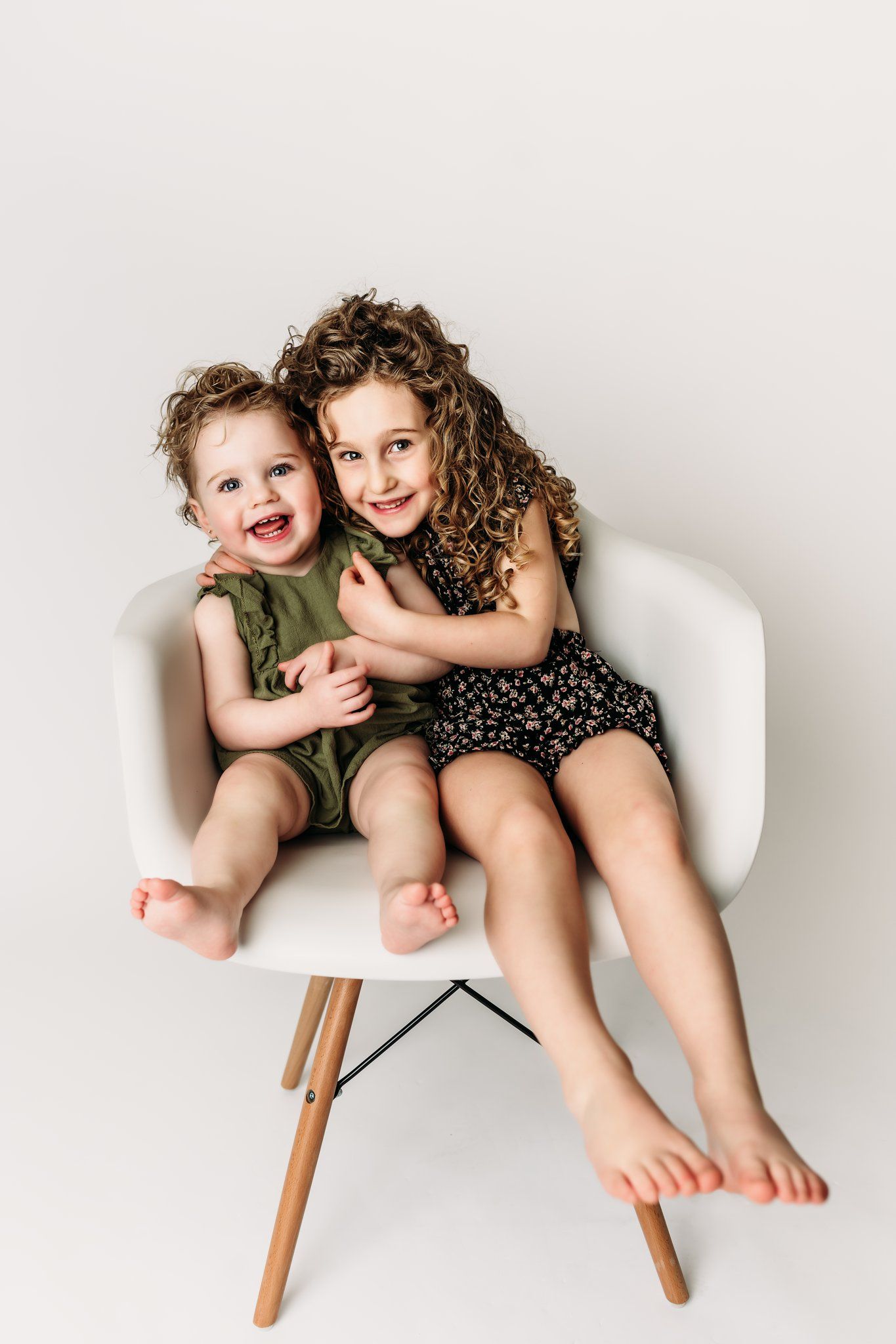 Two children share a sweet moment together while sitting in a white Eames-style chair.