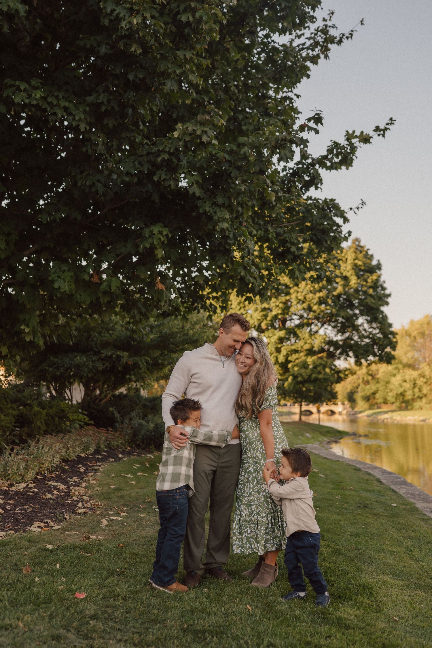 Family playing together outdoors near a lake during golden hour sunset on a grassy hill.
