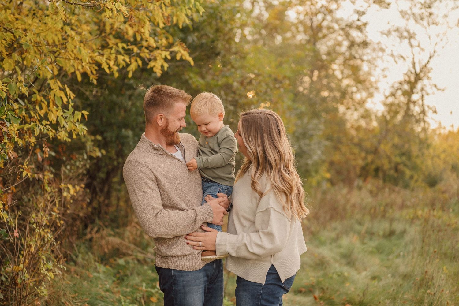 Family enjoying a tender moment together in a sunlit autumn field during golden hour.