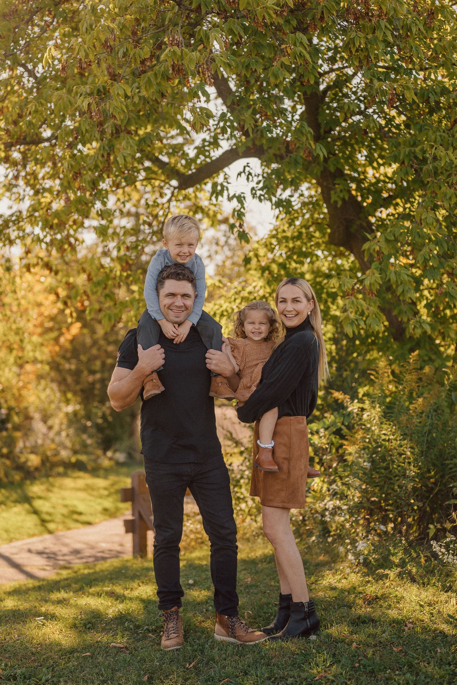 A playful outdoor family photoshoot in a park with golden autumn foliage.