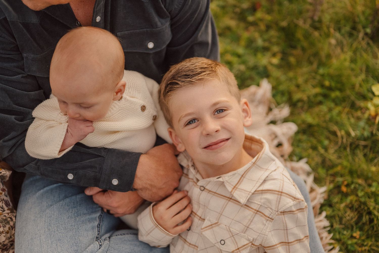Two children sitting together outdoors in autumn wearing light colored shirts with fall foliage in background.