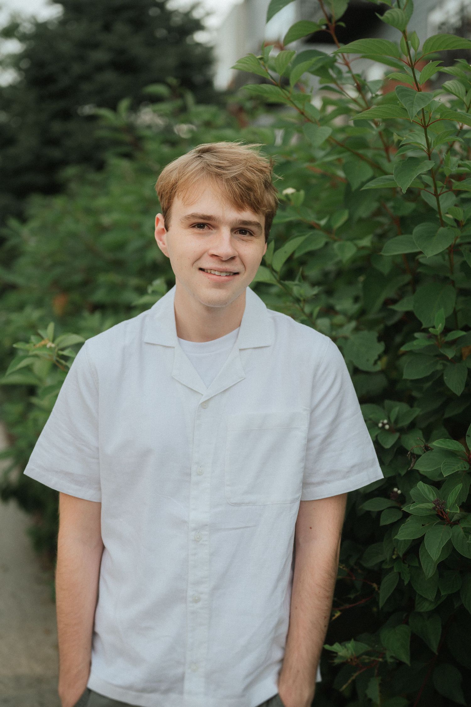 Portrait series in a garden setting wearing a white short-sleeved shirt against green foliage.