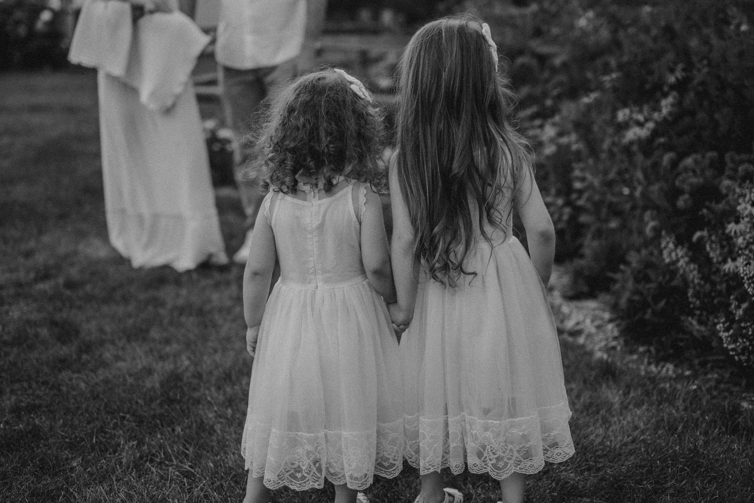 Two white dresses seen from behind against a garden backdrop with hanging laundry.