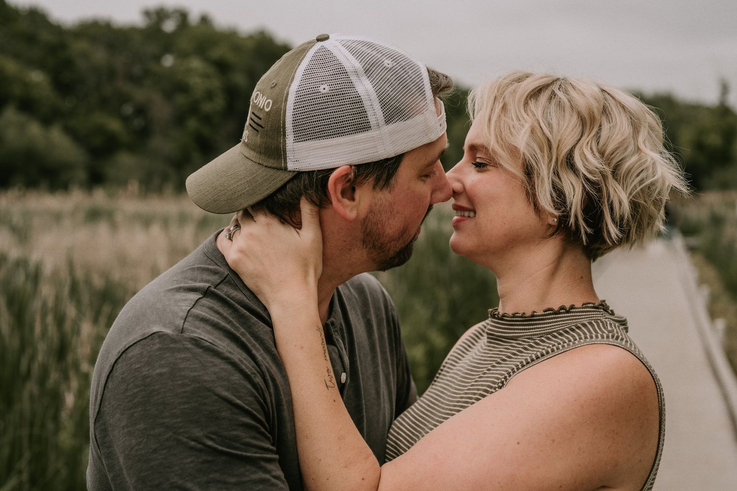 Intimate moment between couple about to kiss on wooden boardwalk surrounded by nature.