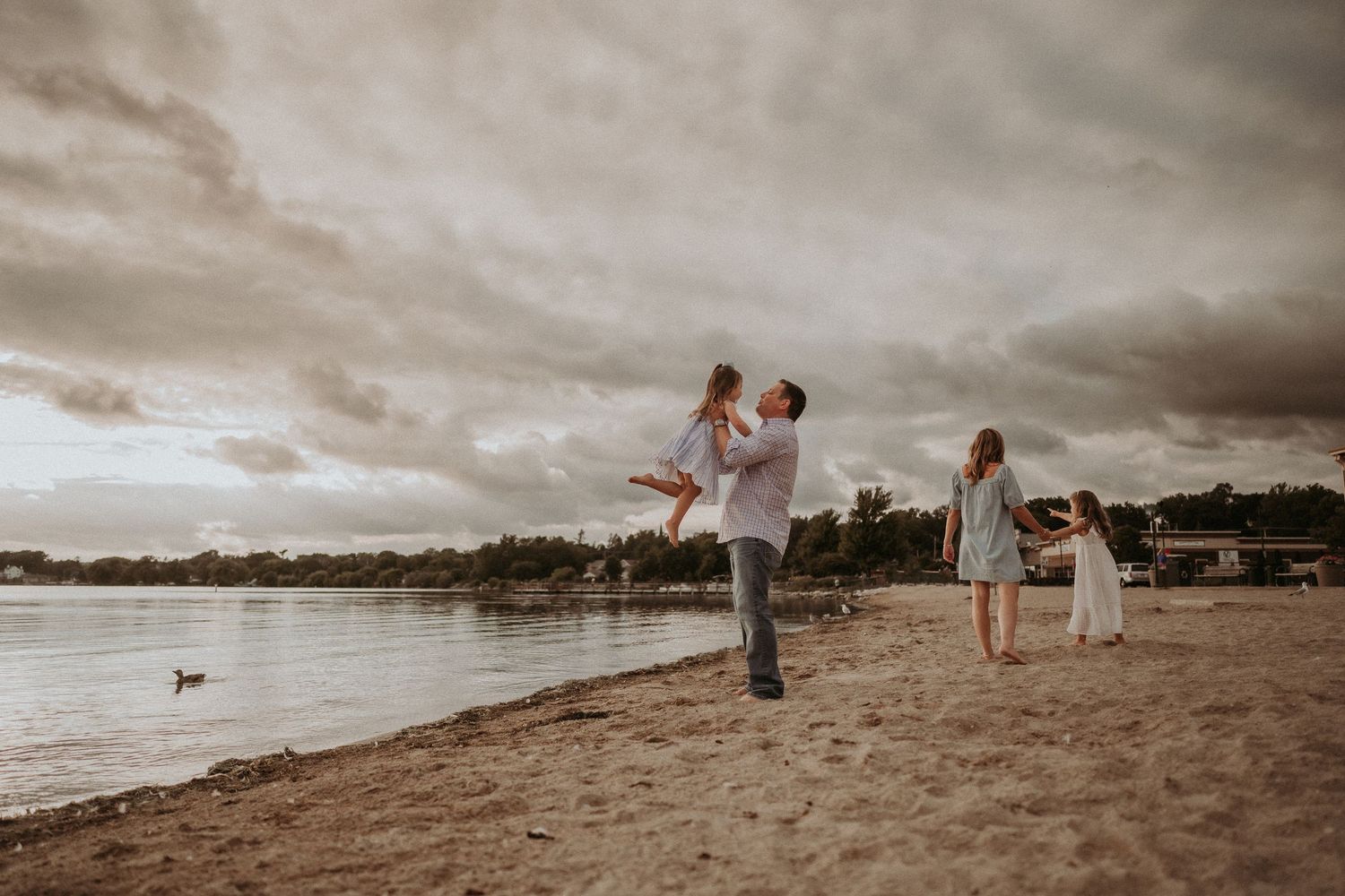 People enjoying playful moments on a beach with dramatic stormy sky in background.