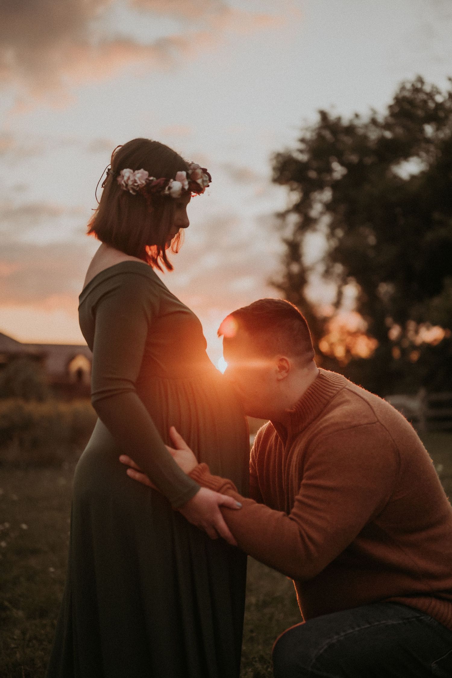Intimate maternity moment captured during sunset in rustic field setting.