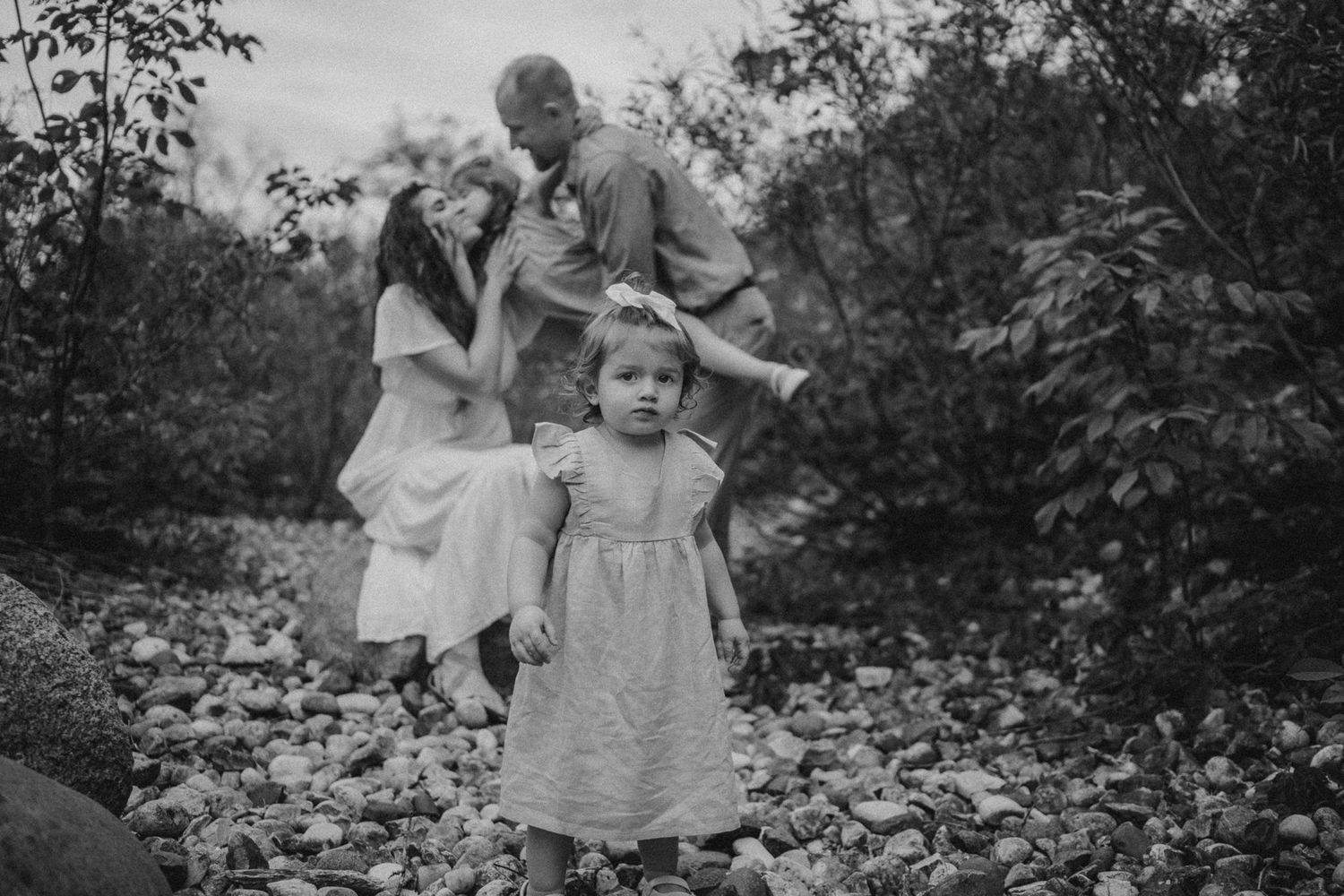 A vintage black and white photograph showing a family moment in a garden with foliage in the background.