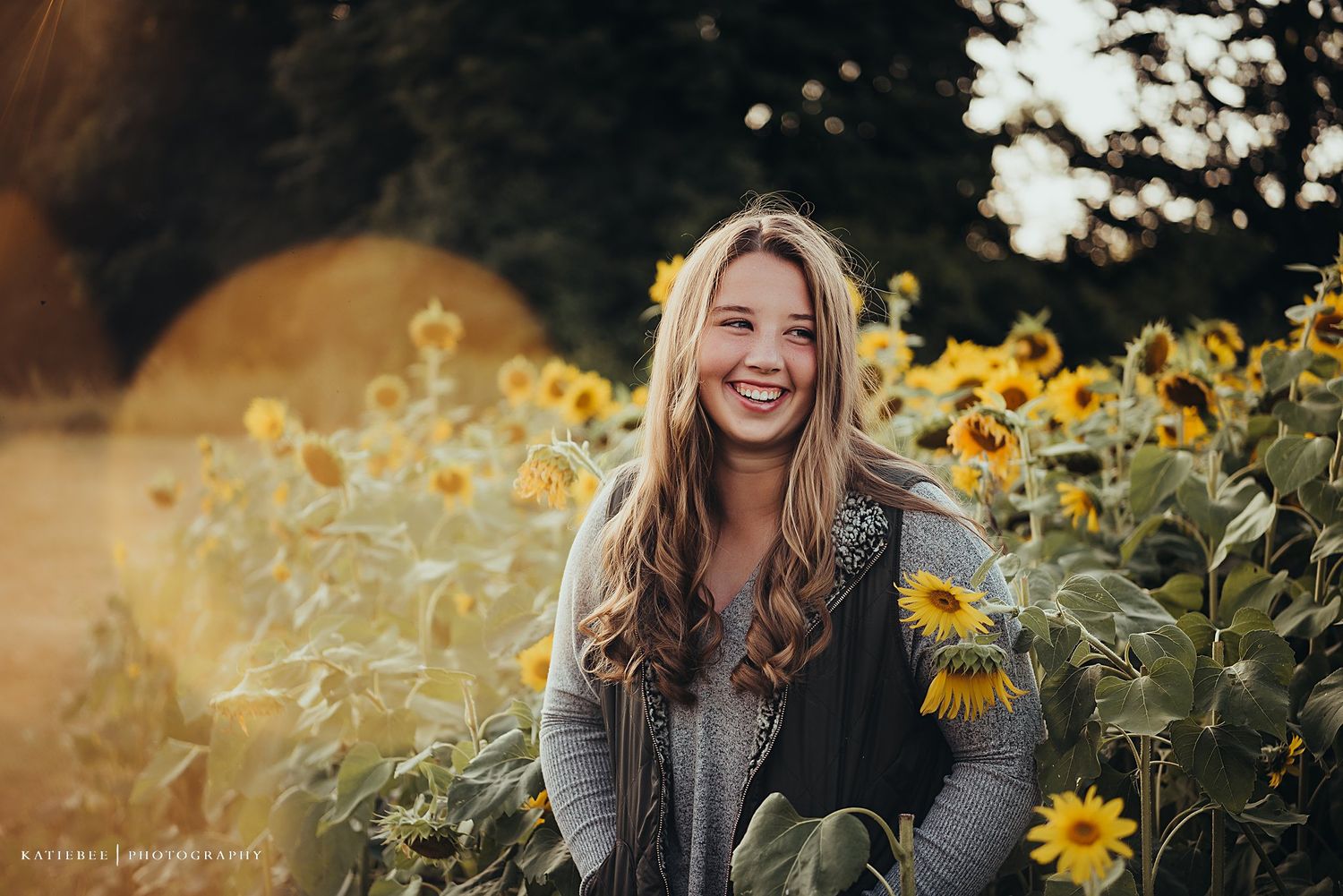 Portrait in sunflower field wearing grey sweater with warm golden sunset lighting.