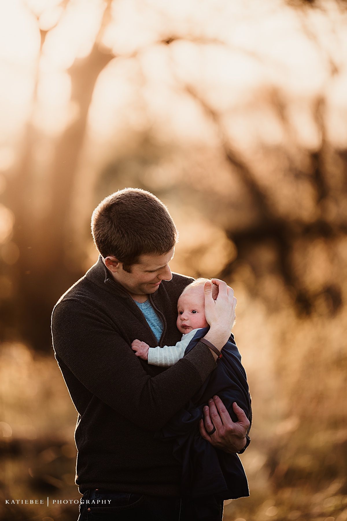 Parent cradles infant during emotional sunset portrait session outdoors.