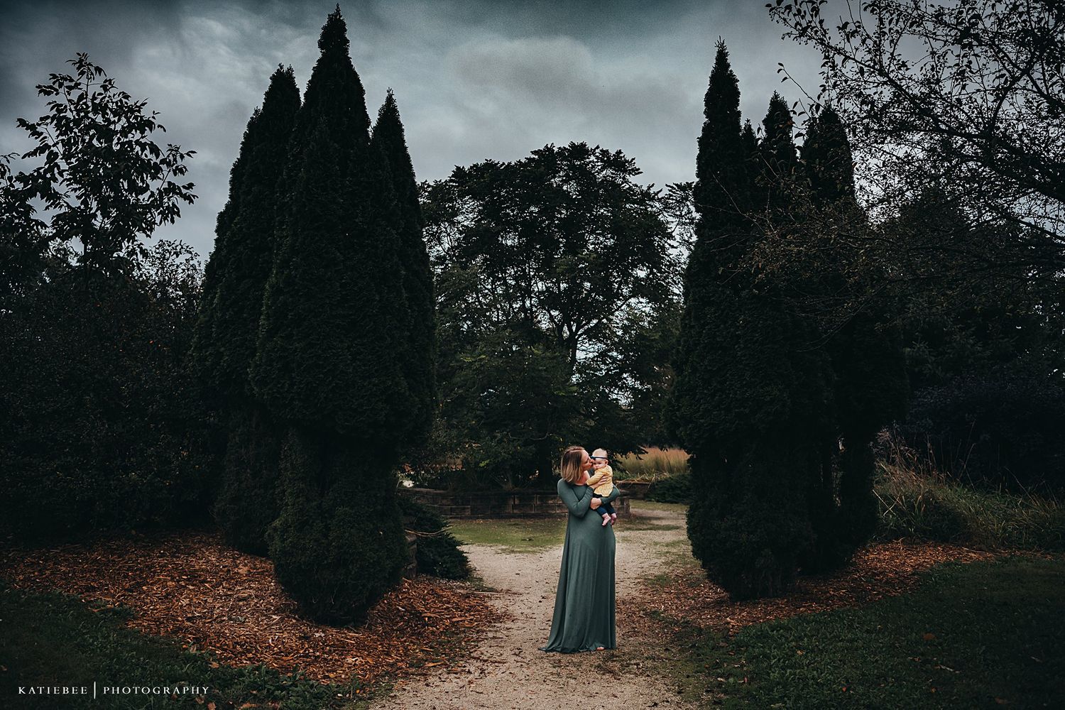A dramatic outdoor portrait against tall cypress trees on a moody cloudy day.