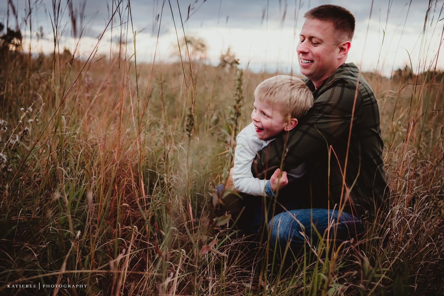 An emotional candid moment between parent and child amid tall grasses at sunset.