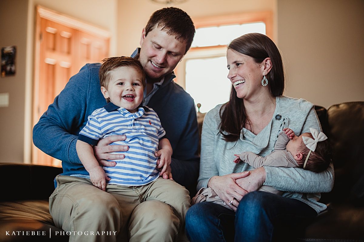 Family relaxing together on dark leather couch during casual indoor photo session.