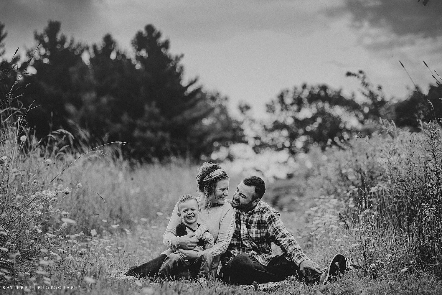 A black and white portrait of two people sitting in a meadow surrounded by tall grass.