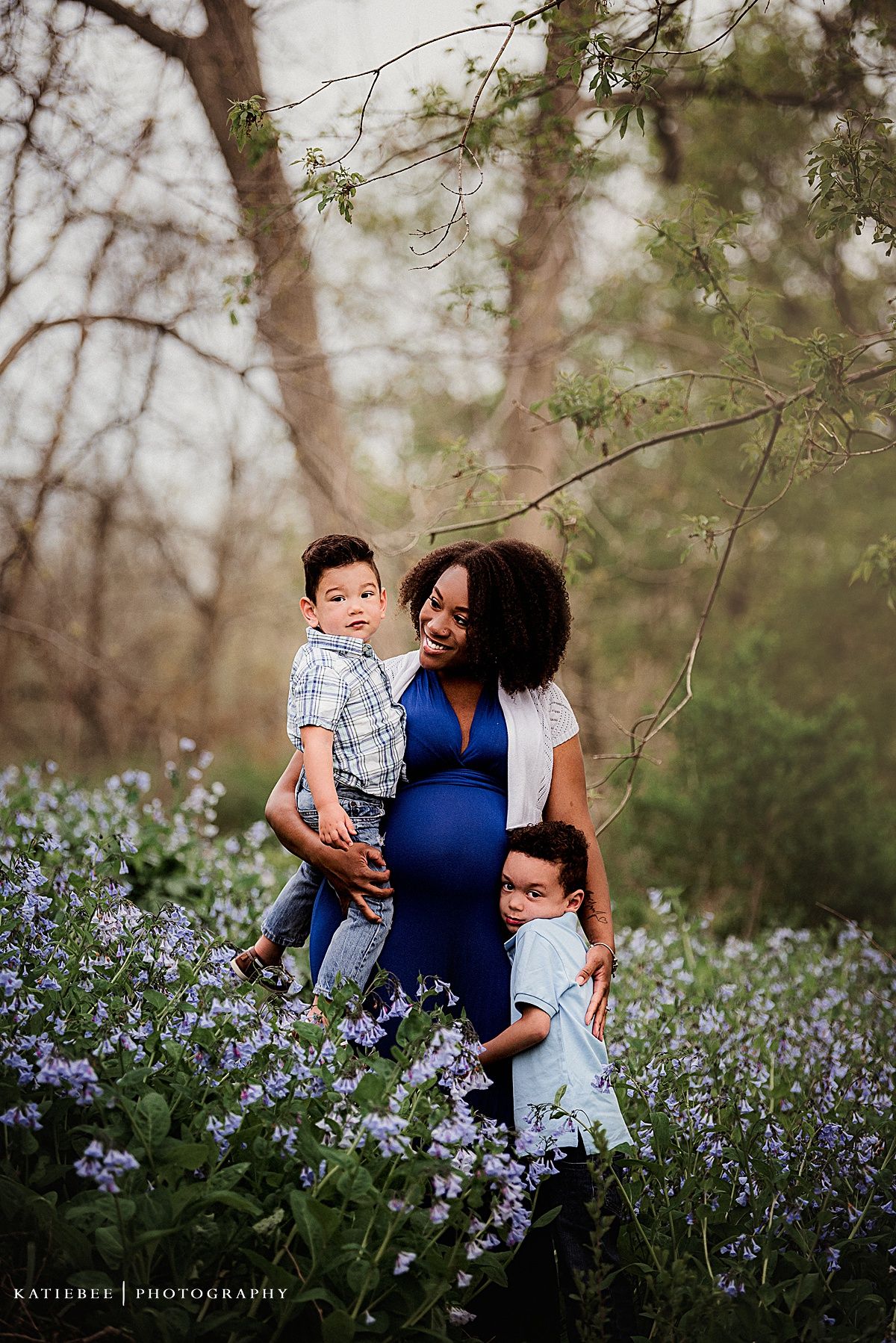 Family maternity photo with children standing in field of purple spring flowers.