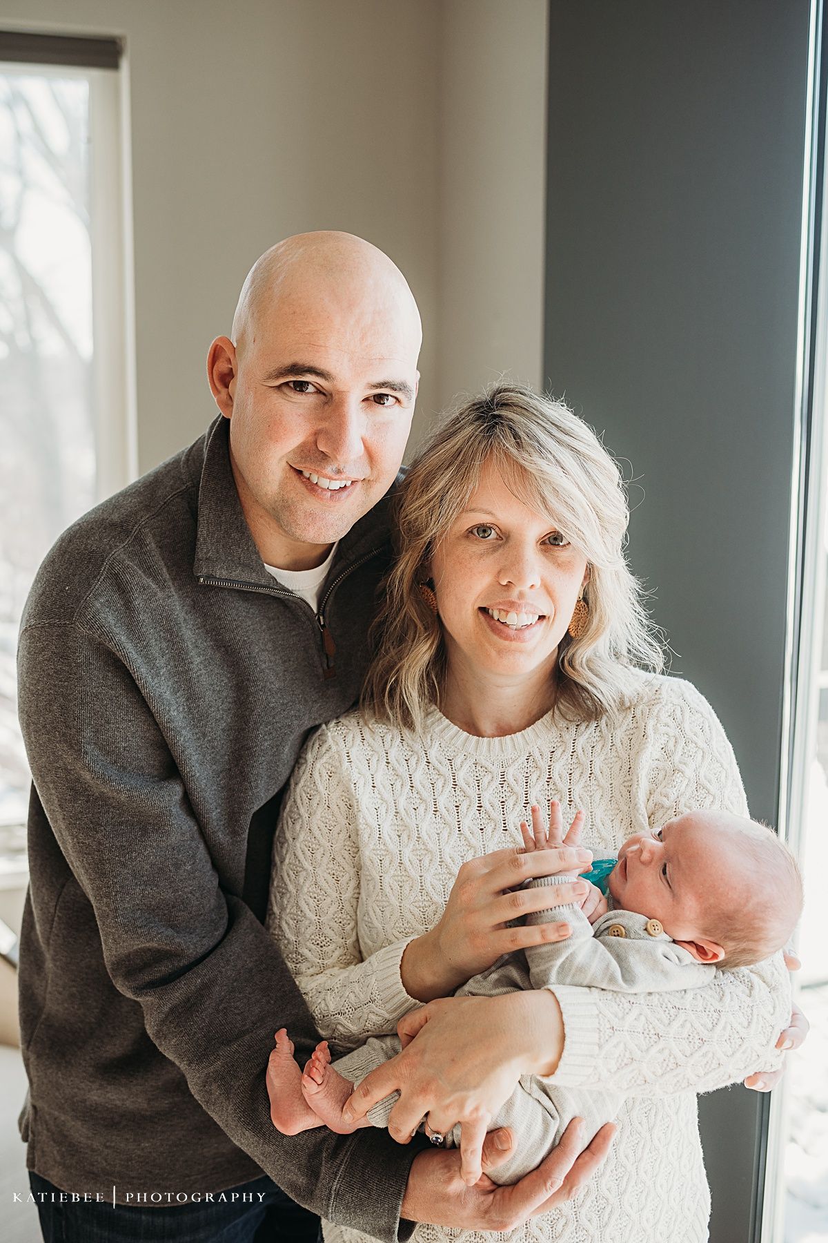 Joyful family portrait with newborn baby by bright window.