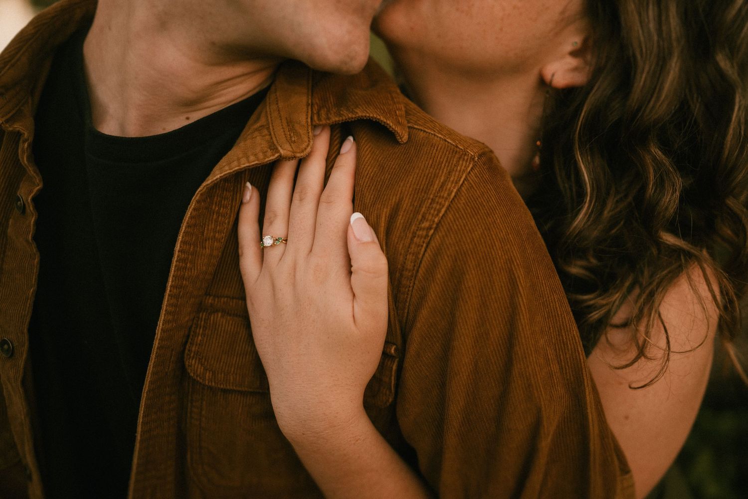 A tender romantic moment captured in warm tones showing hands embracing against a brown corduroy jacket.