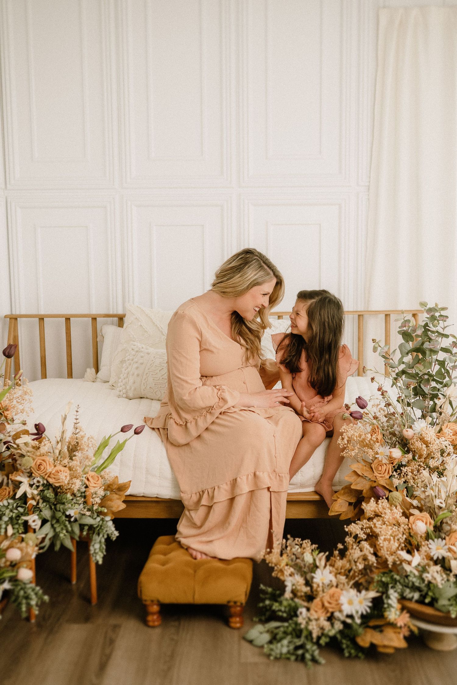 Parent and child share an intimate moment on wooden bench surrounded by romantic peach and cream floral arrangements.