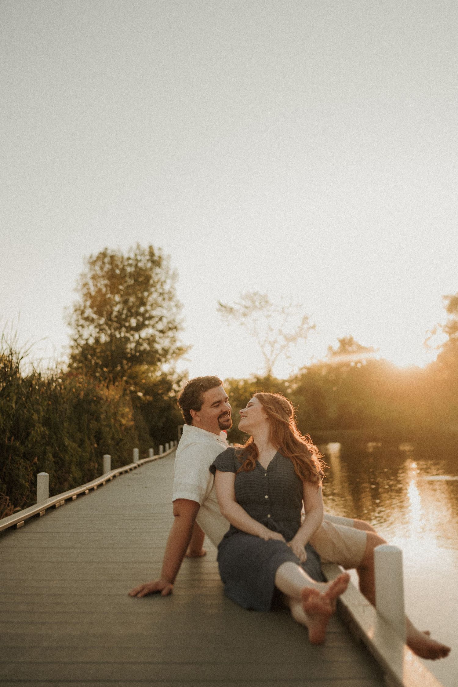 A couple shares a romantic moment on a wooden boardwalk during golden hour.