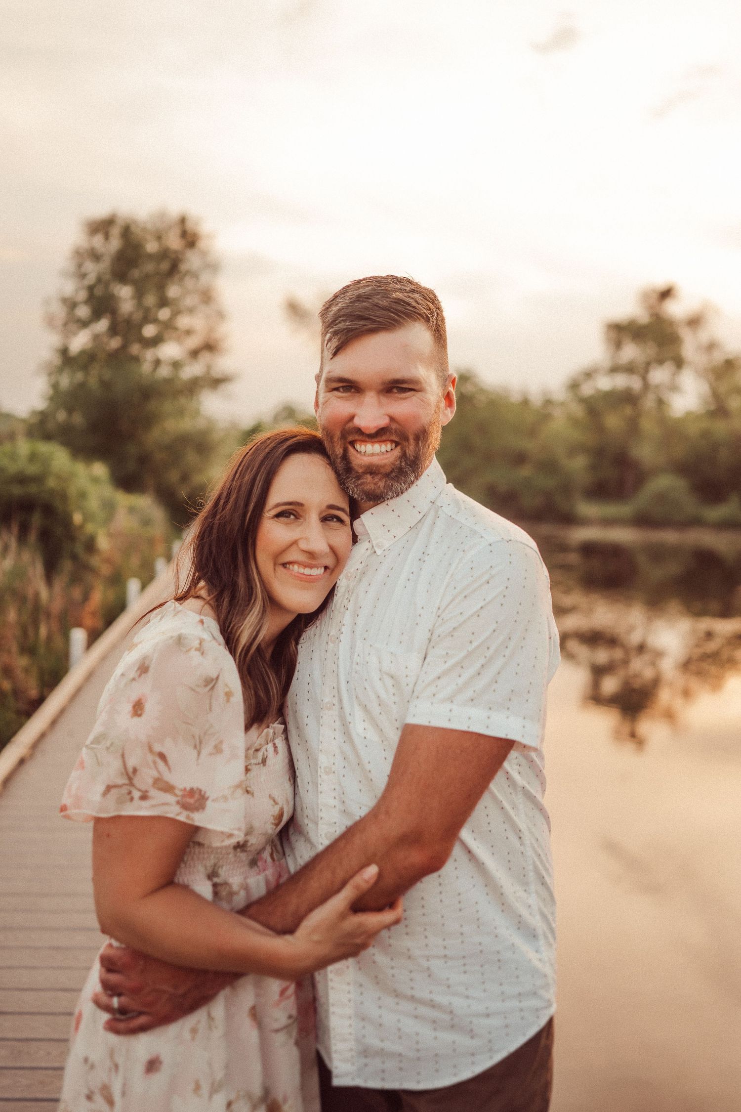 Couple sharing a joyful embrace on wooden dock during golden hour.