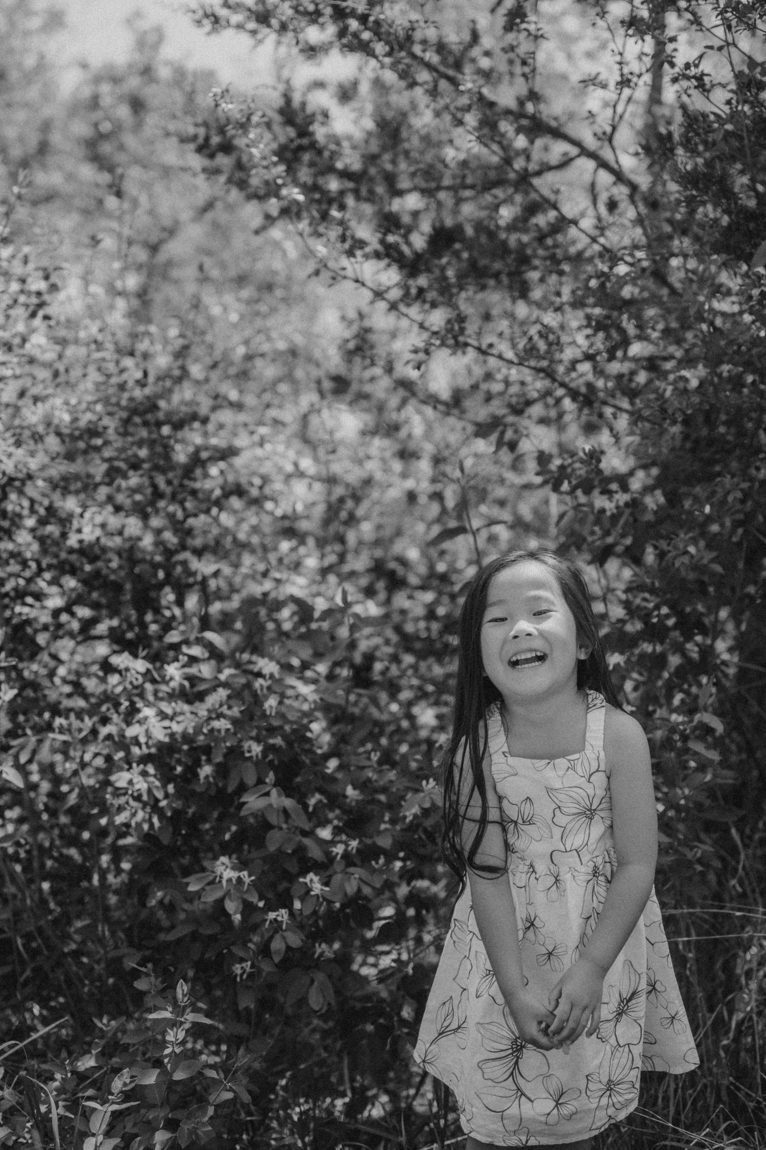 A black and white portrait showing joy and laughter against a leafy natural background.