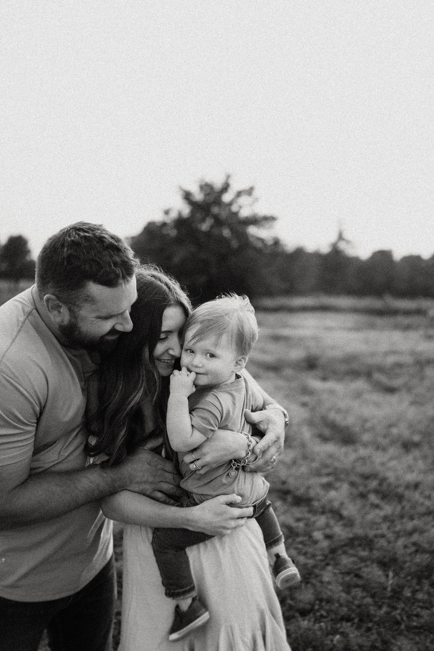A black and white portrait of a family sharing an intimate moment outdoors.