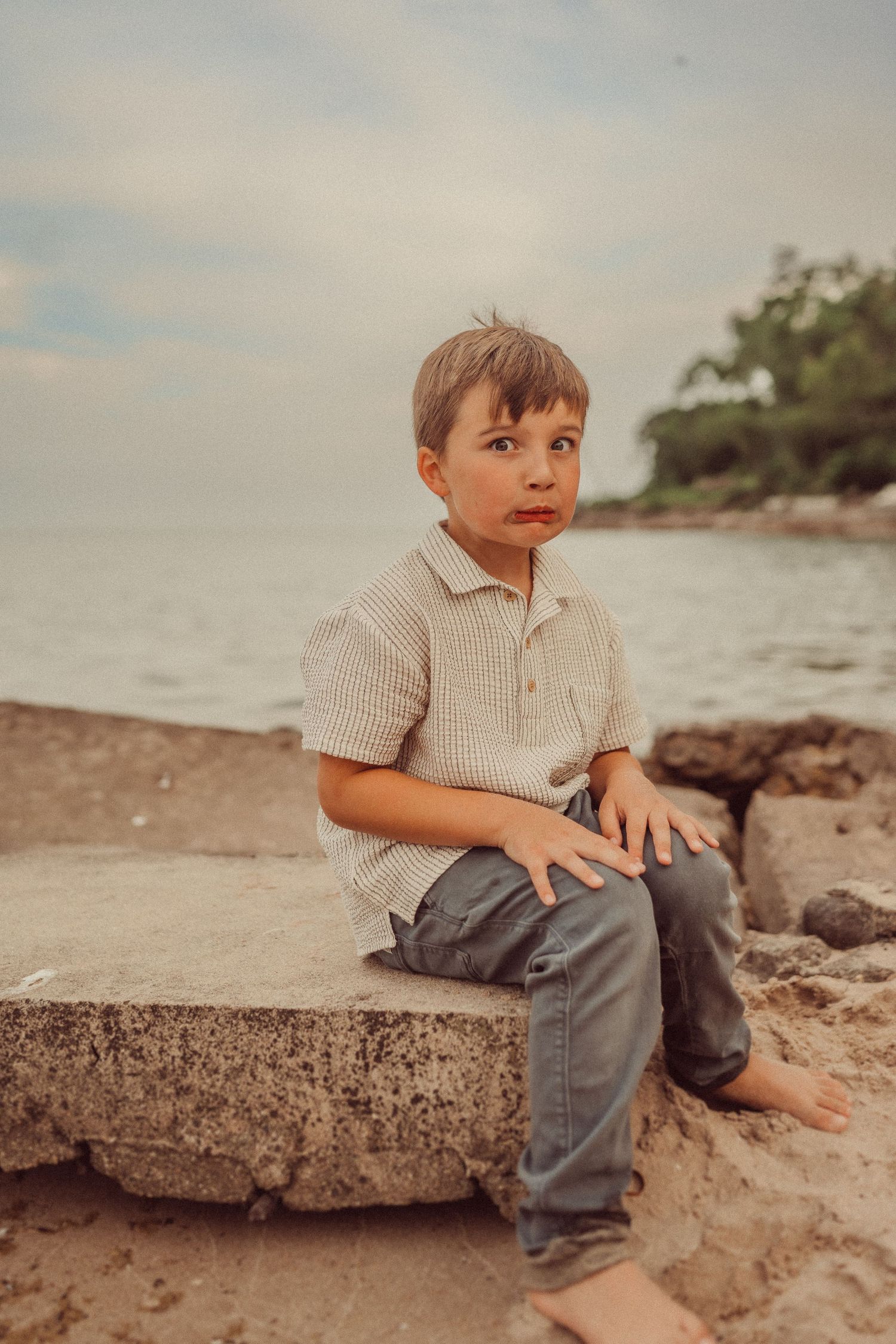 A thoughtful moment captured of someone sitting barefoot on a stone block by the water.