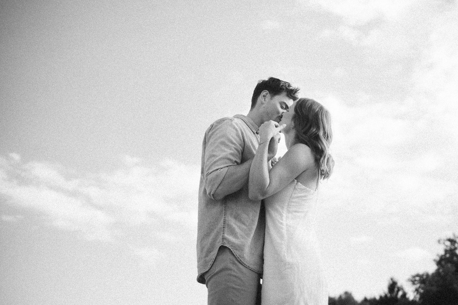A couple embraces in a romantic moment against a bright sky during golden hour.