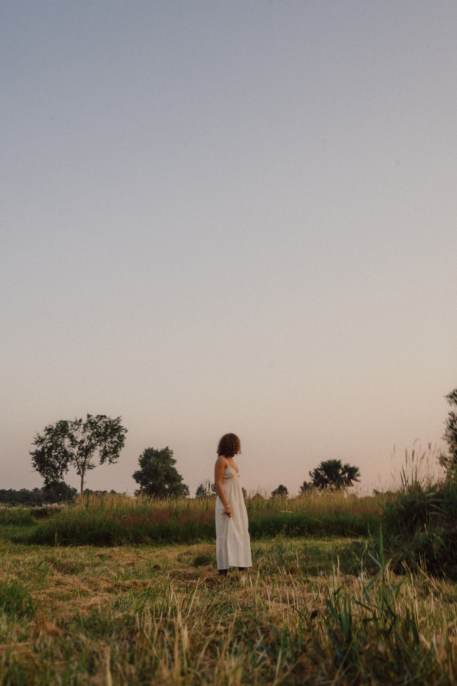 Ethereal silhouettes of figures in white dresses walking through a misty field at dusk.