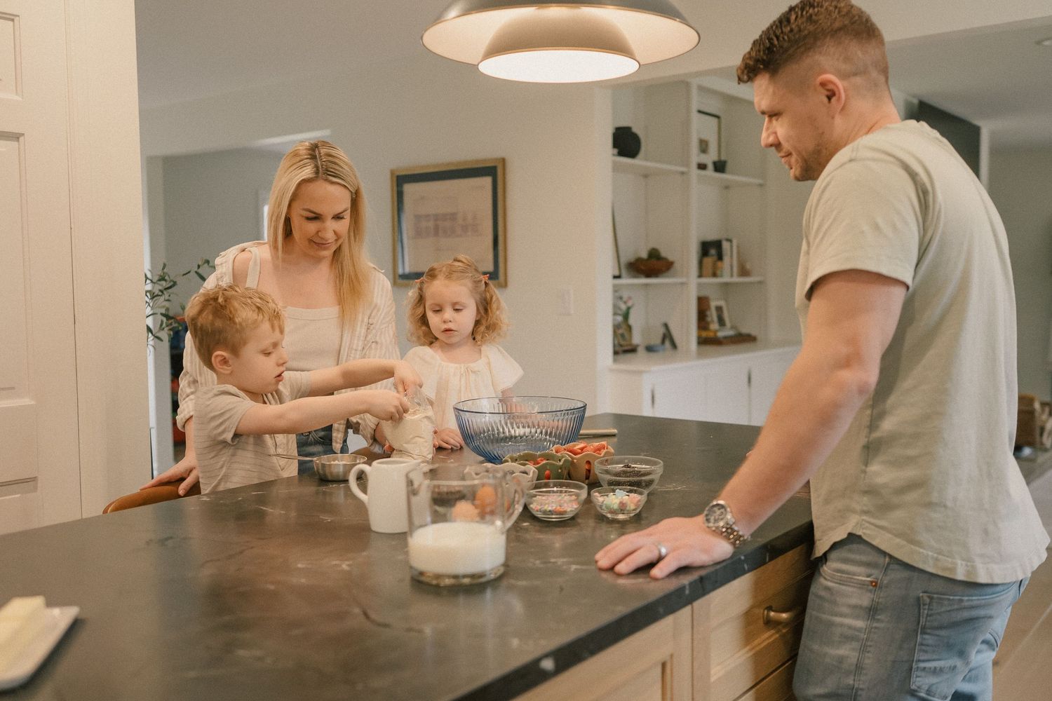 Family of four baking together at kitchen island with bowls and ingredients.