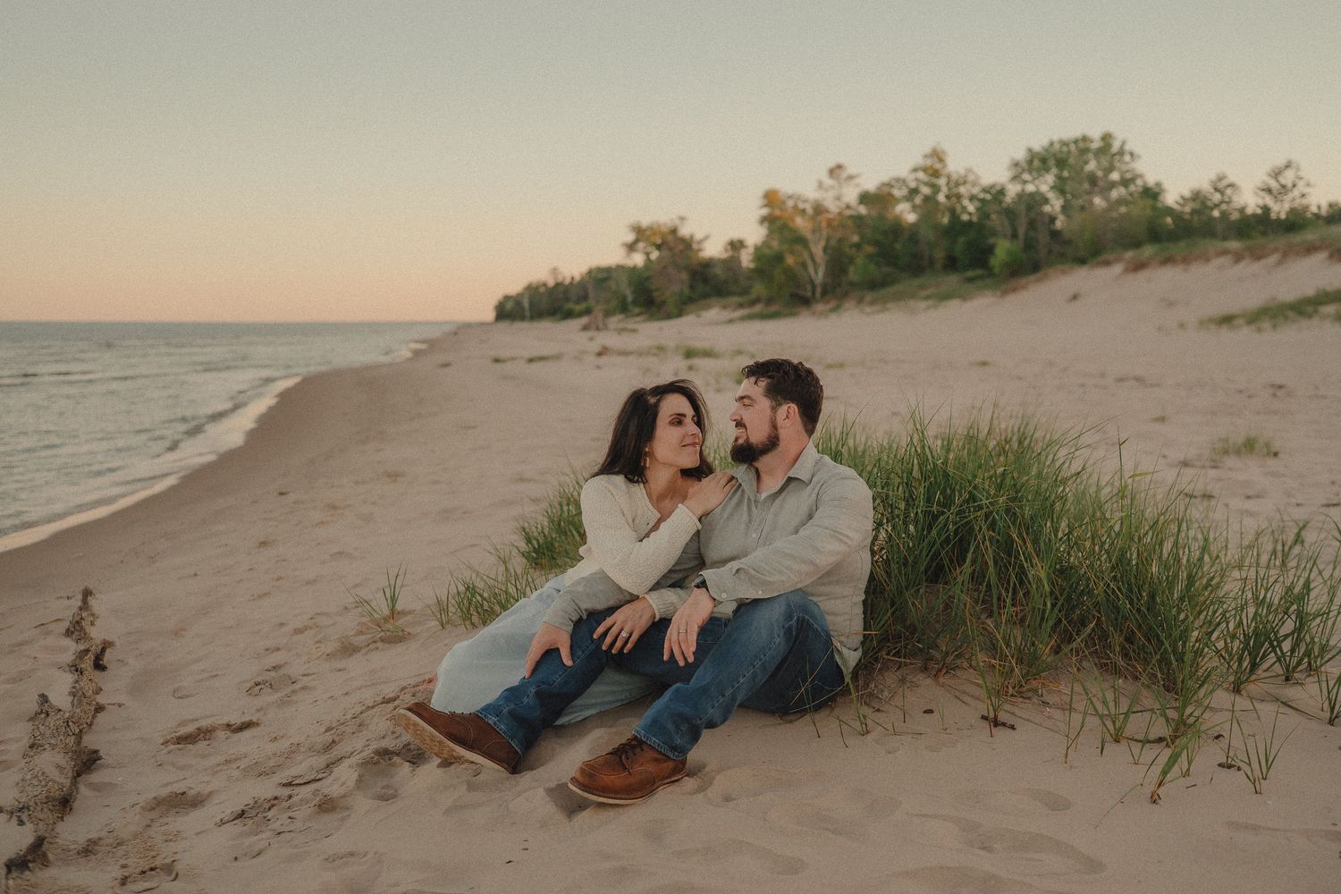Couple sitting together on sandy beach dunes at golden sunset gazing lovingly at each other.