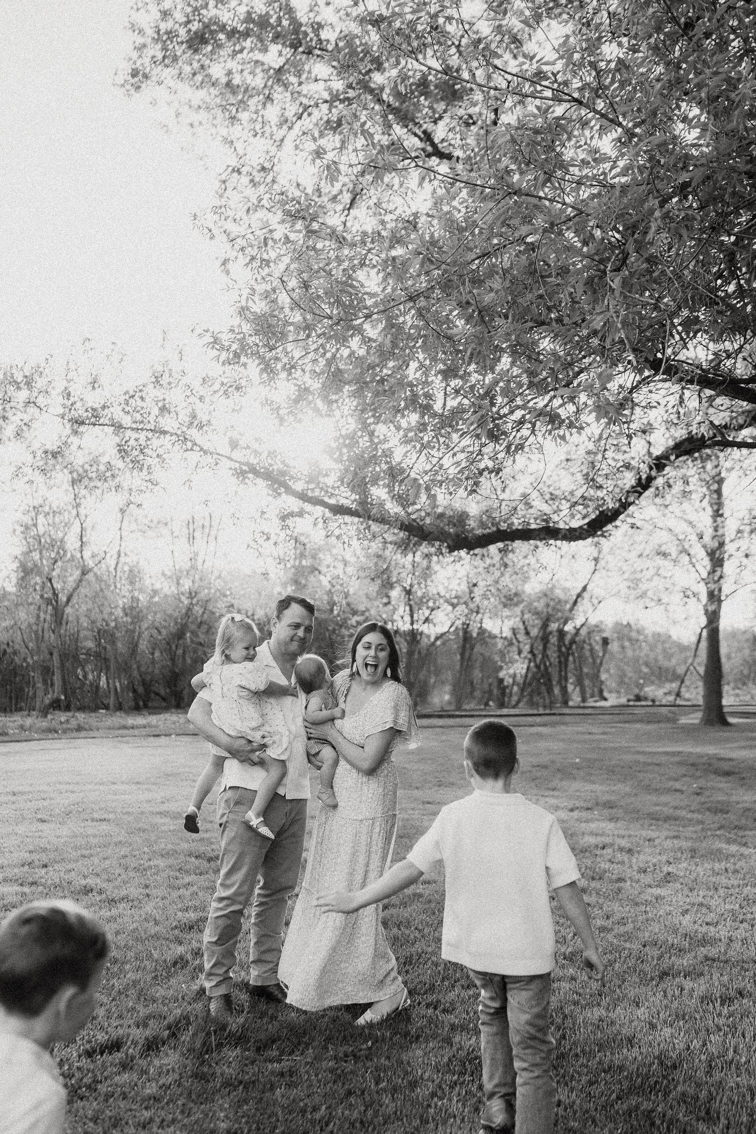 Black and white photo of a family playing outdoors under a large tree on a grassy lawn.