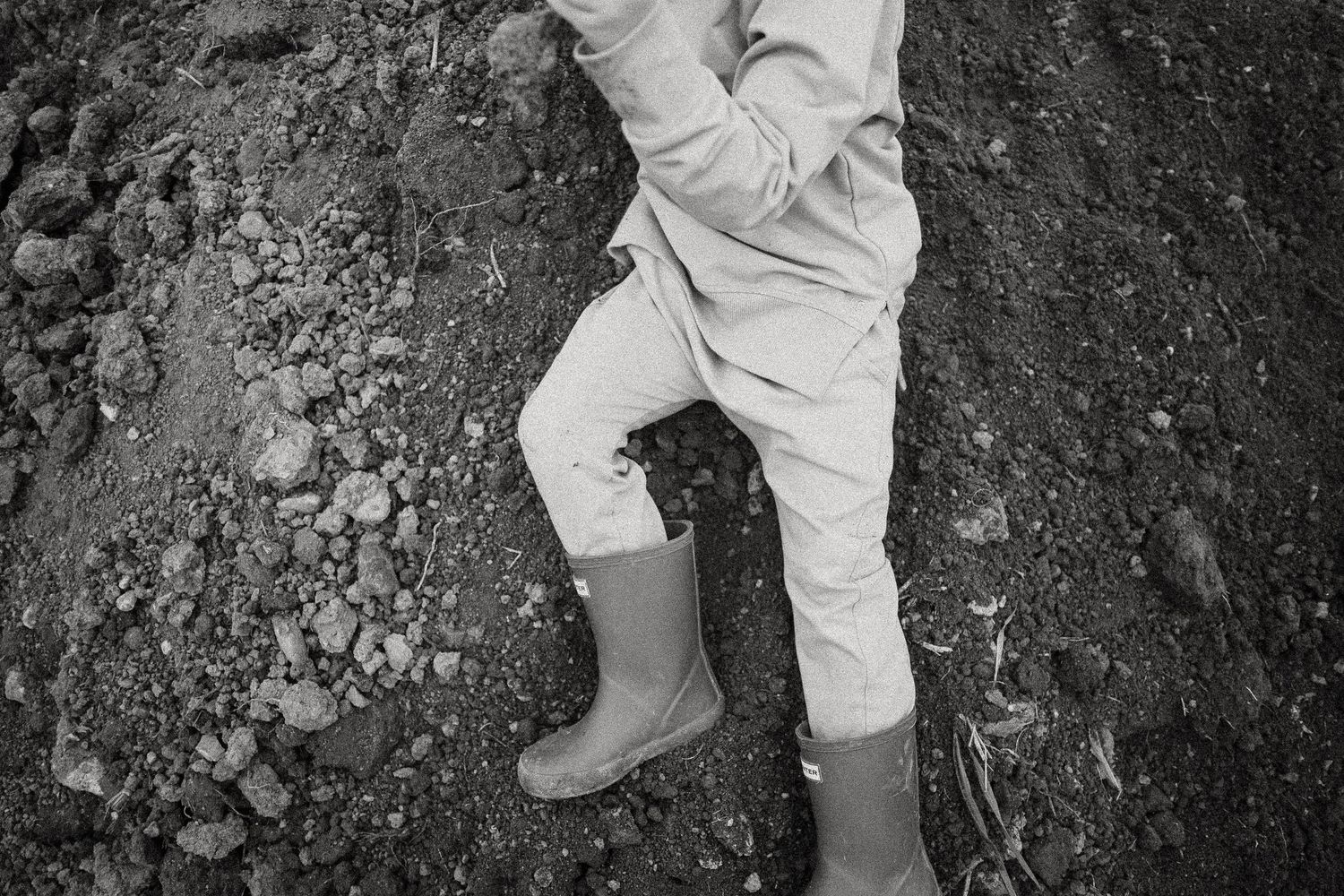 Child wearing rubber boots standing on rocky soil in black and white photo.