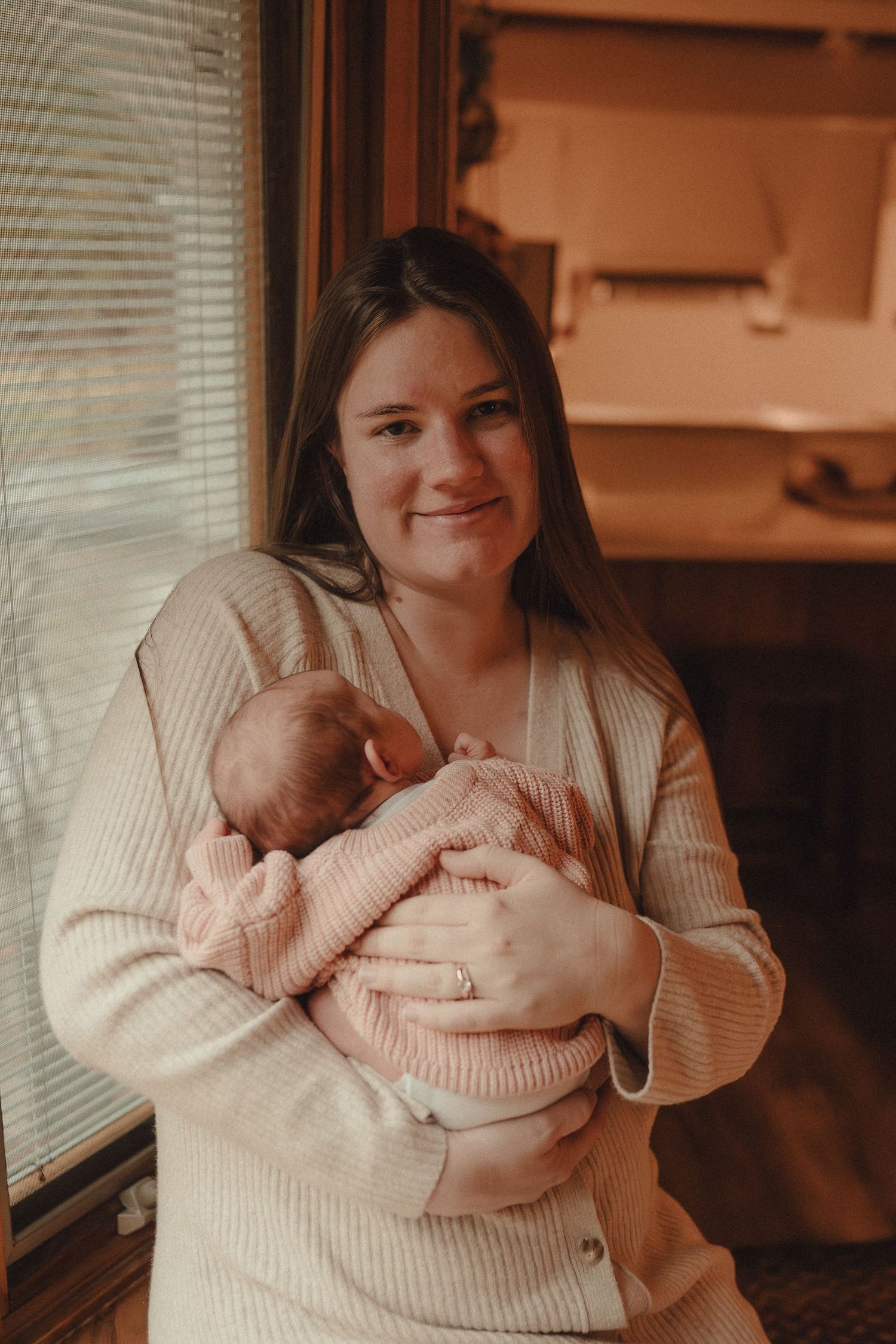 Warm-toned lifestyle photos capturing sweet moments between parent and newborn by window.