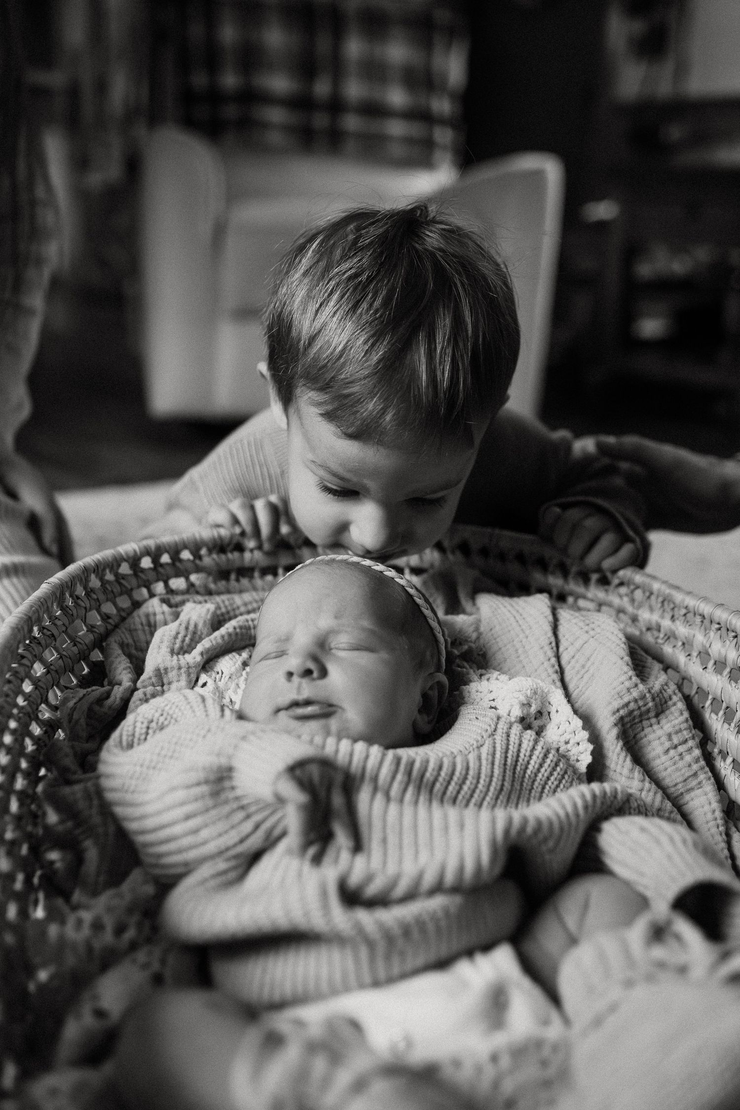 Black and white photo of siblings sharing a tender moment on textured blanket.