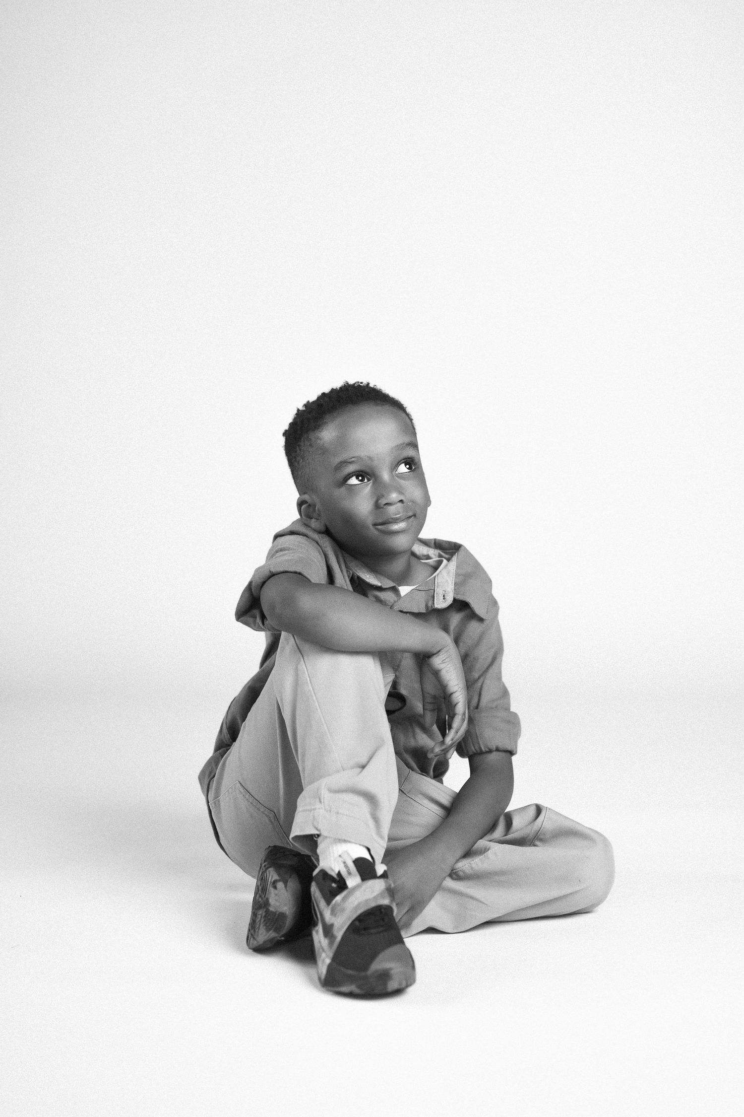 A child in gray clothing sits and plays with a small kitten in a bright studio setting.
