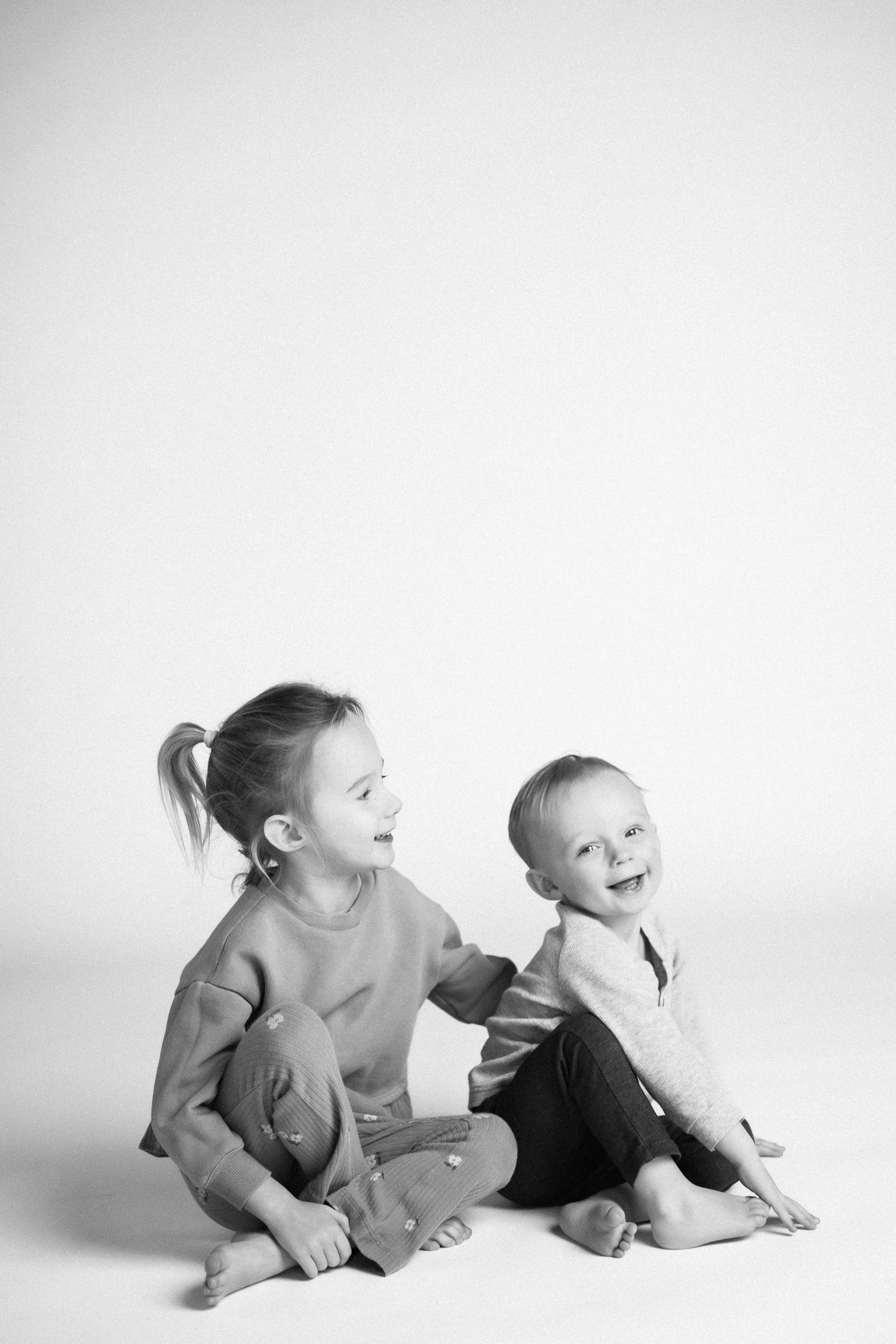 Two children laying on their stomachs laughing and playing together on white backdrop.