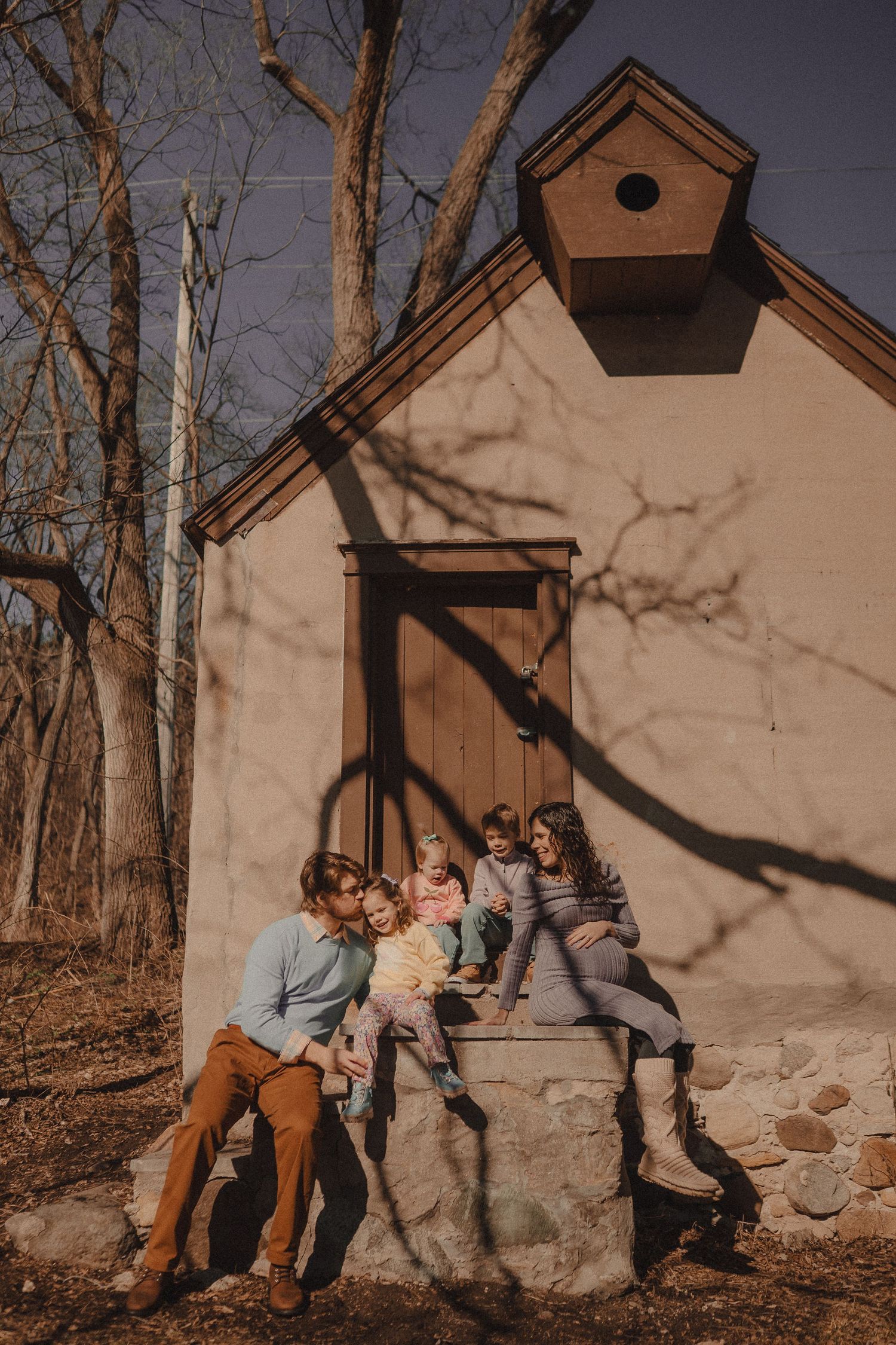 Children playing and posing against a beige building with a birdhouse in warm afternoon light.