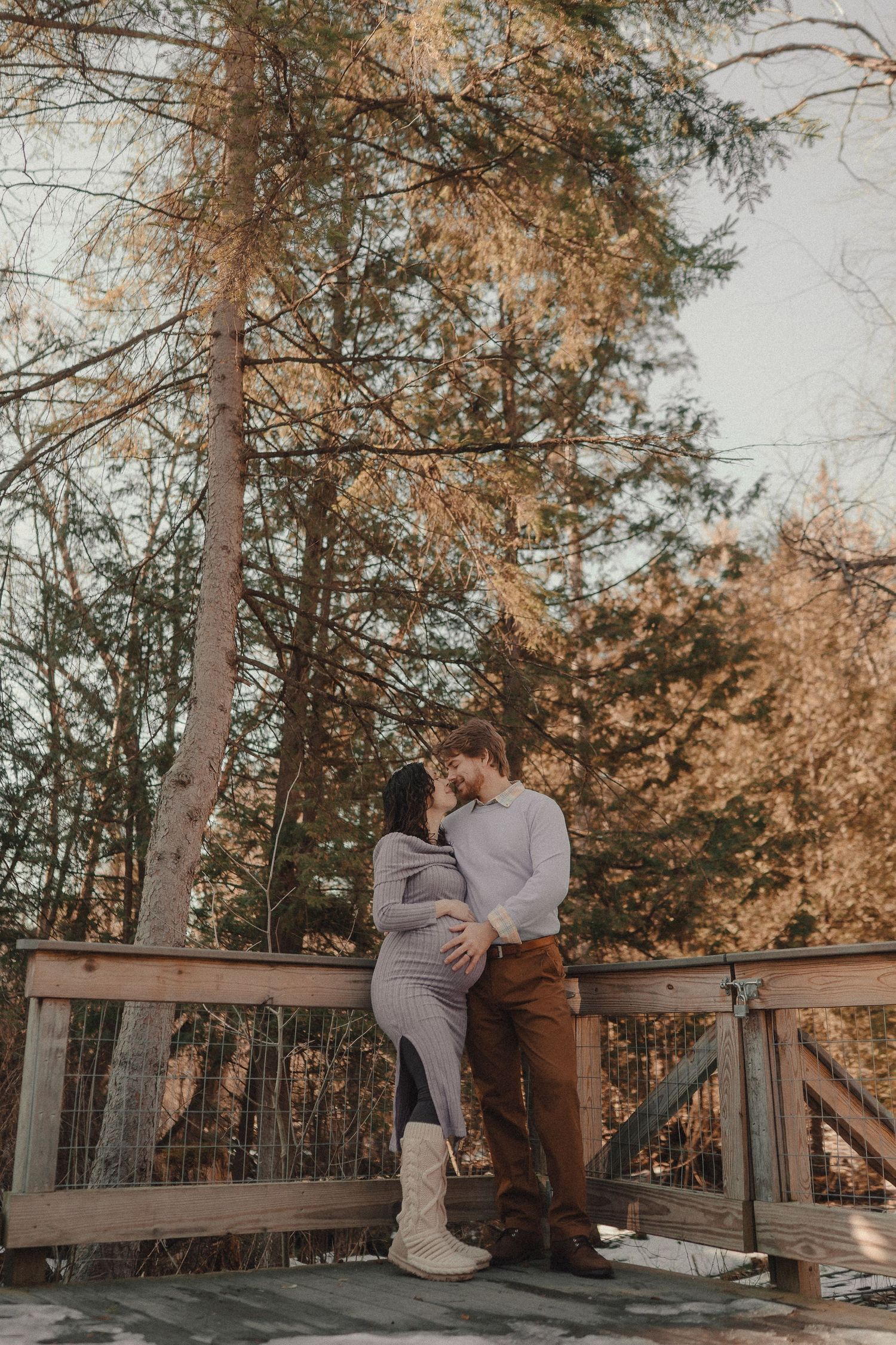 A couple shares tender moments on a wooden deck surrounded by tall pine trees during golden hour.
