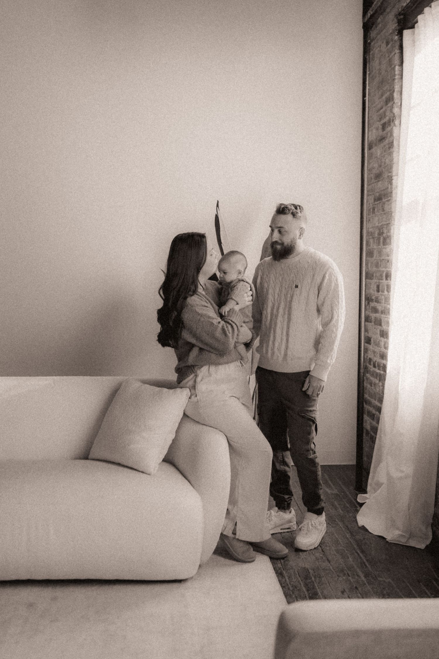 Black and white photo series showing intimate family moments on a minimalist white couch against brick walls.