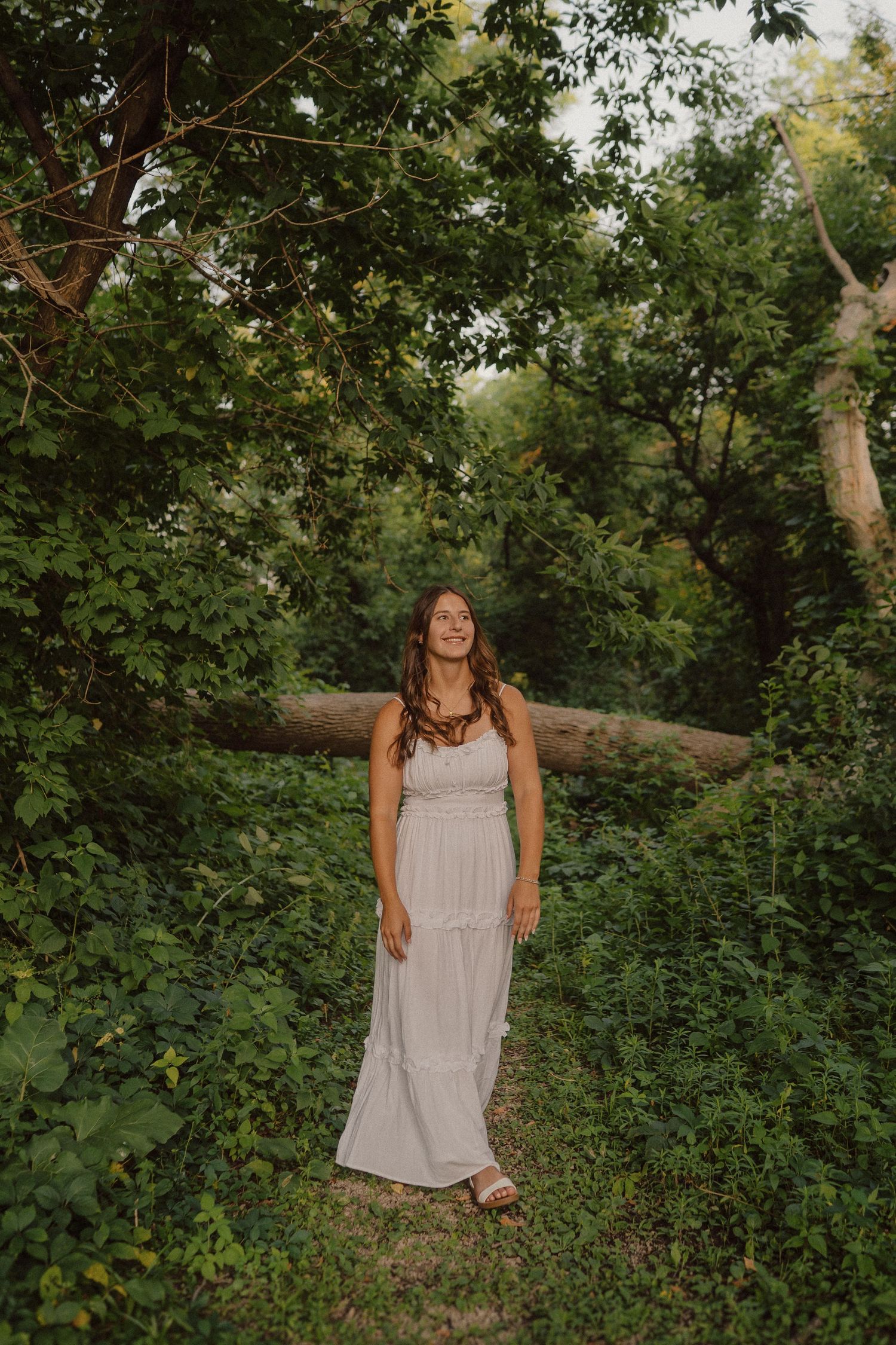 White sundress contrasts beautifully against lush green forest setting in golden hour lighting.