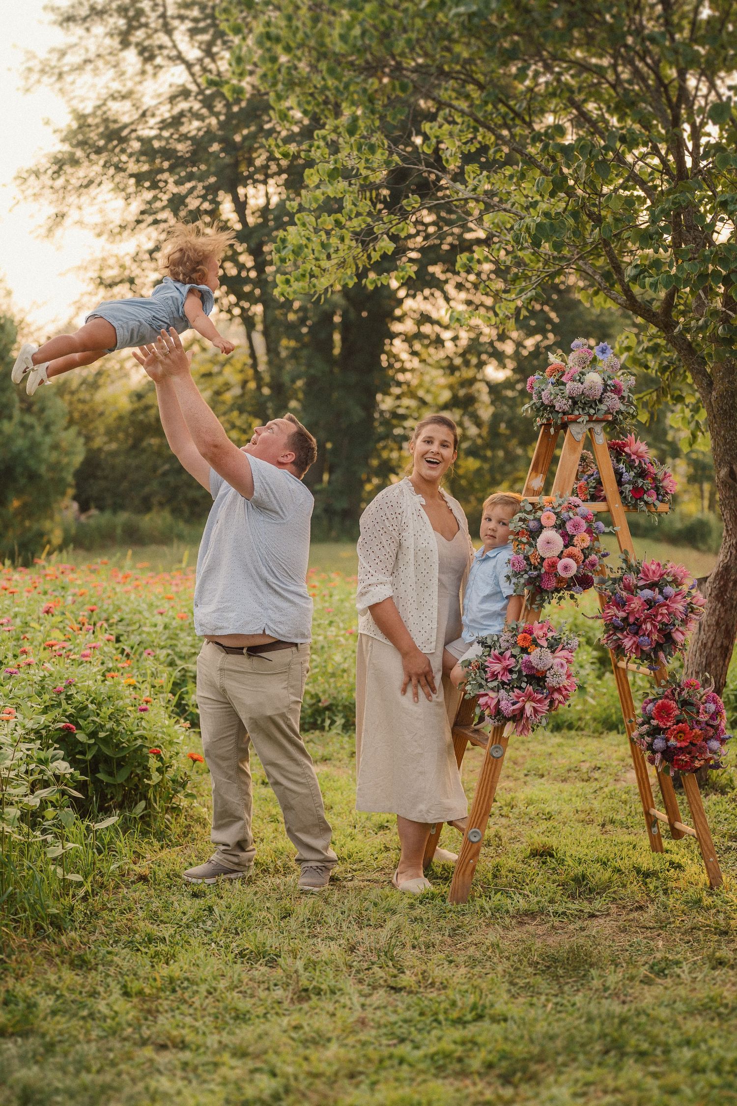 A joyful outdoor family photoshoot with beautiful floral decorations on a wooden ladder in a garden at sunset.