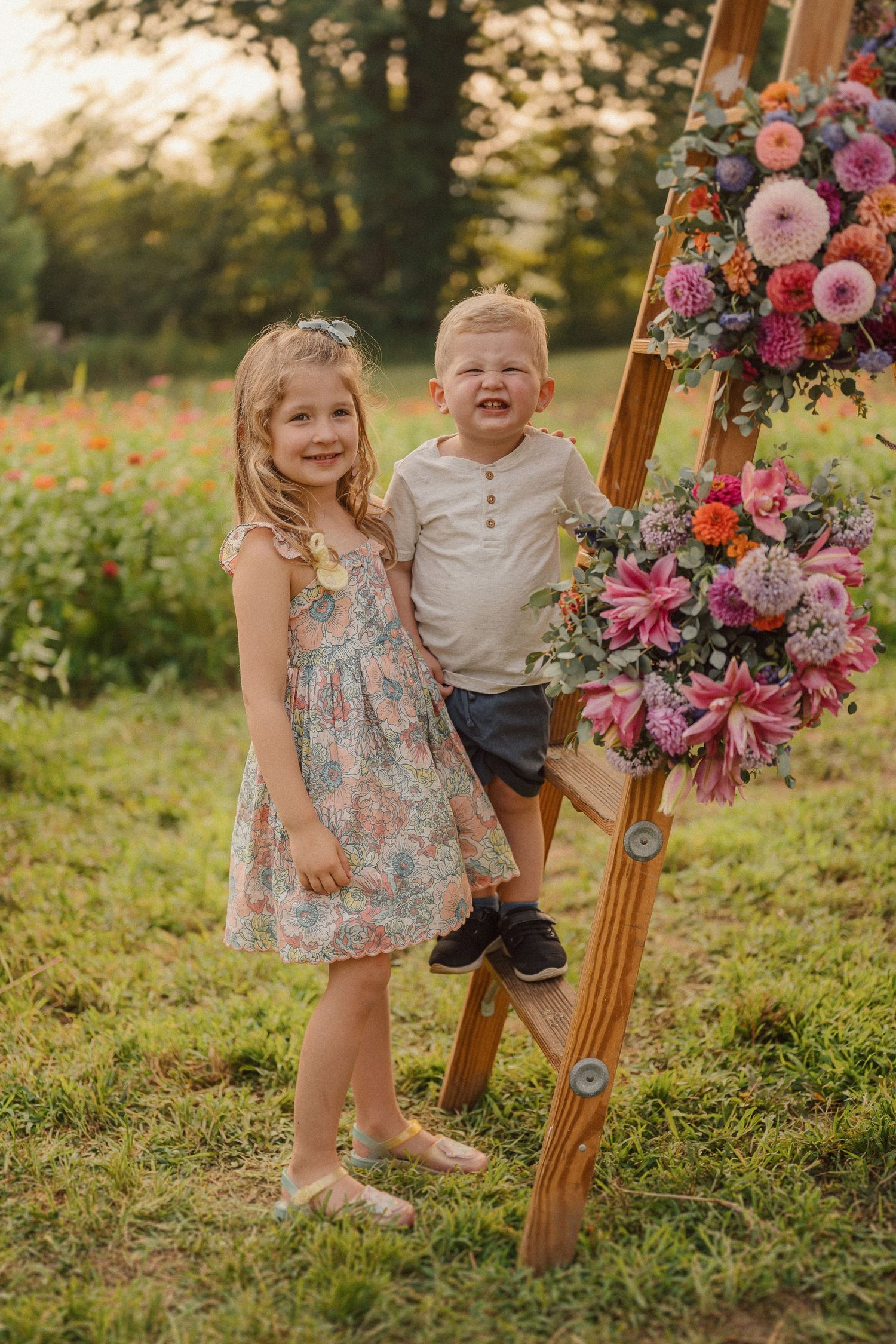 Children playing at sunset near a wooden ladder decorated with vibrant pink and purple floral arrangements.