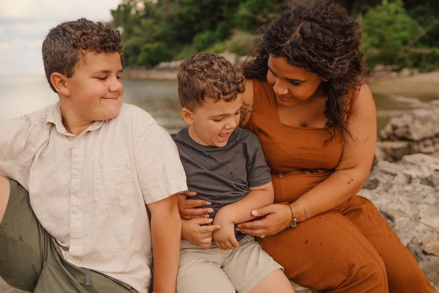 Family enjoys warm bonding moments sitting together by the rocky shore at sunset in nature.